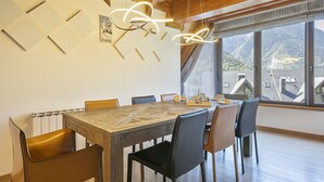 A dining area with a wooden table, chairs, a modern light fixture, and a view of the outdoors. - Luderna - Dúplex Sant Marti XII (Gessa)