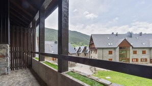 A balcony with stone flooring, wooden railings, and a view of traditional buildings with sloped roofs and wooden shutters. - Luderna - Casa con terraza Somont (Naut Aran)