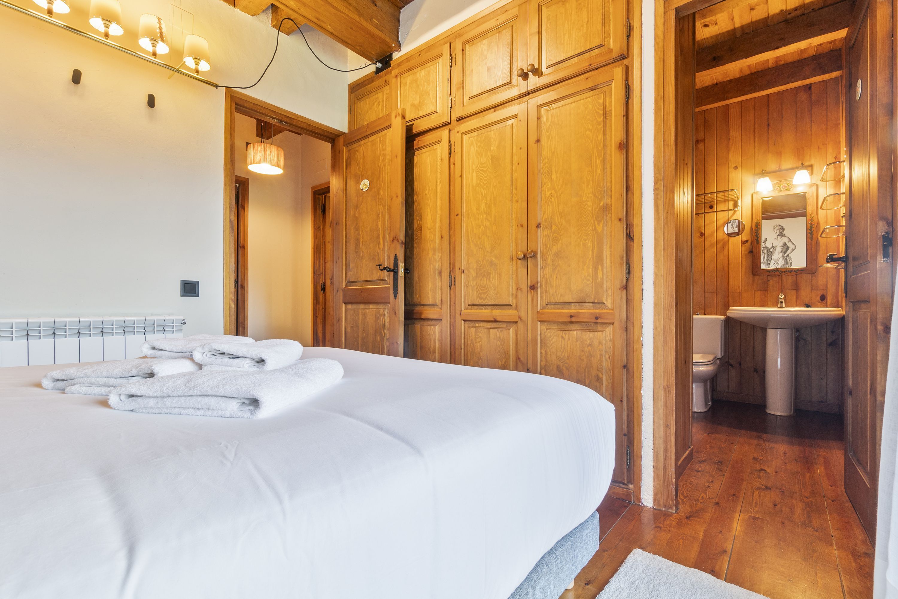 Une chambre avec un grand lit, une armoire en bois et une salle de bain équipée d’un lavabo et de toilettes.