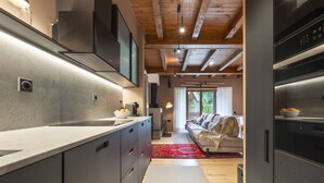 A modern kitchen with a large island, built-in appliances, and a view into a living area with a sofa and a window. - Luderna - Casa con terraza Somont (Naut Aran)