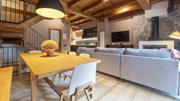 A modern living room with a wooden dining table, gray sofa, and a stone fireplace. - Luderna - Casa con terraza Somont (Naut Aran)