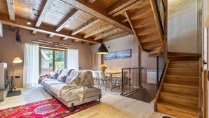 A spacious living area with a wooden ceiling, a sofa, a dining table, and a staircase. - Luderna - Casa con terraza Somont (Naut Aran)