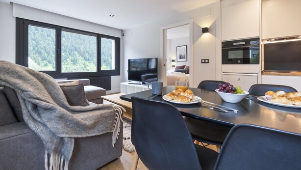 A modern living room with a sofa, a dining table with chairs, a TV, and a kitchen area with appliances. - Luderna - Apartamento Misharnon (Baqueira)