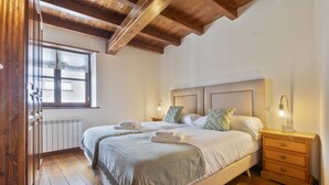 A bedroom with a large bed, wooden floor, a window with blinds, a bedside table with a lamp, and a radiator. - Luderna - Apto con terraza Rouche (Arties)