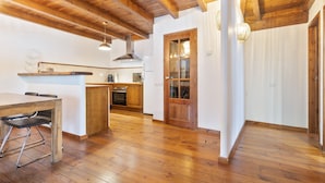 A spacious kitchen with wooden beams, a dining area with a table and chairs, and a glass-fronted door leading to another room. - Luderna - Apto con terraza Rouche (Arties)