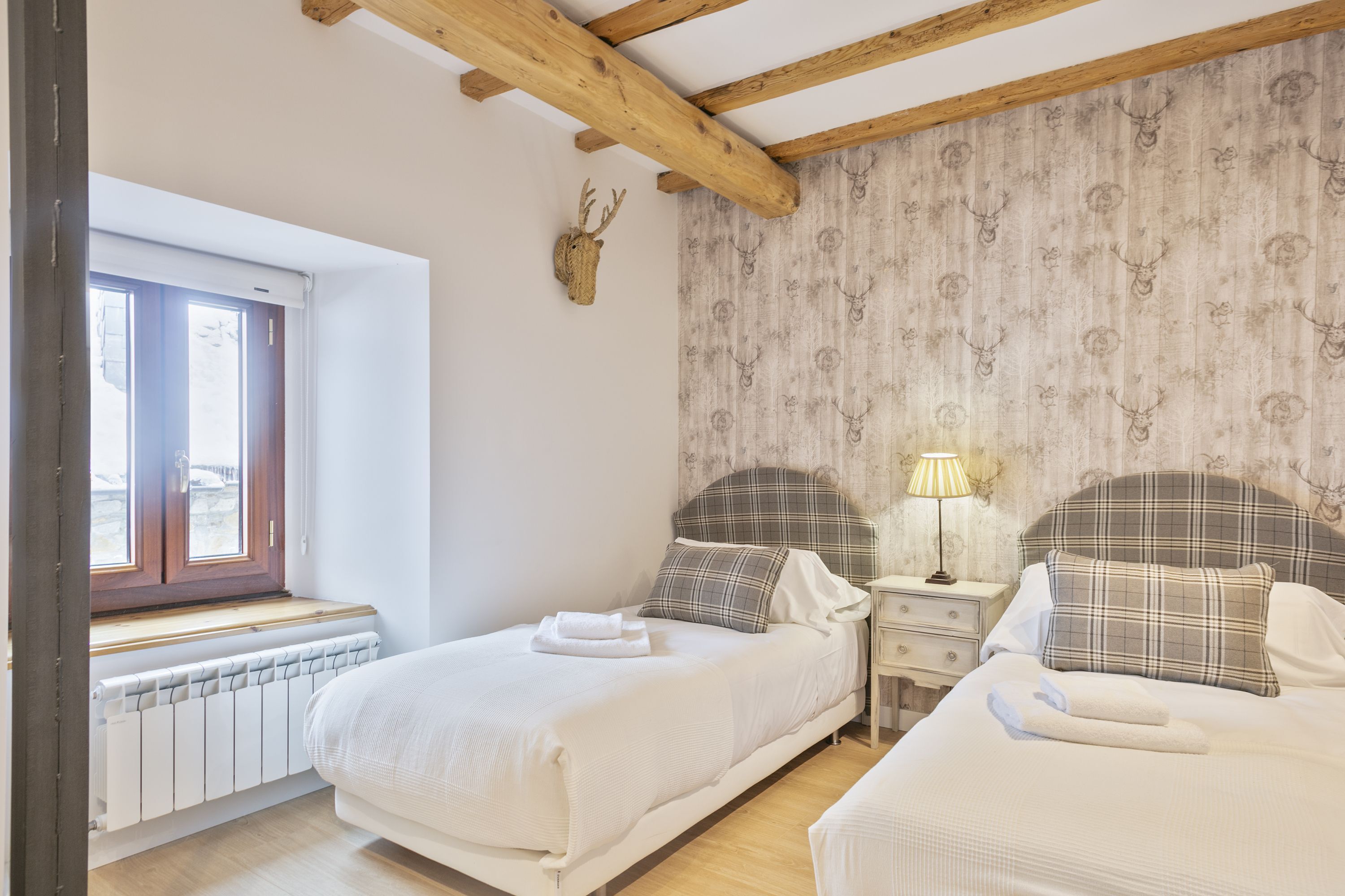 Une chambre avec deux lits, une fenêtre, un radiateur et une décoration murale représentant une tête de cerf.