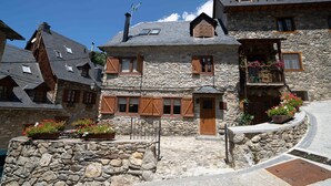 Ein Steinhaus mit Holzhörnern, einem Balkon mit Blumen und einer Steintreppe.