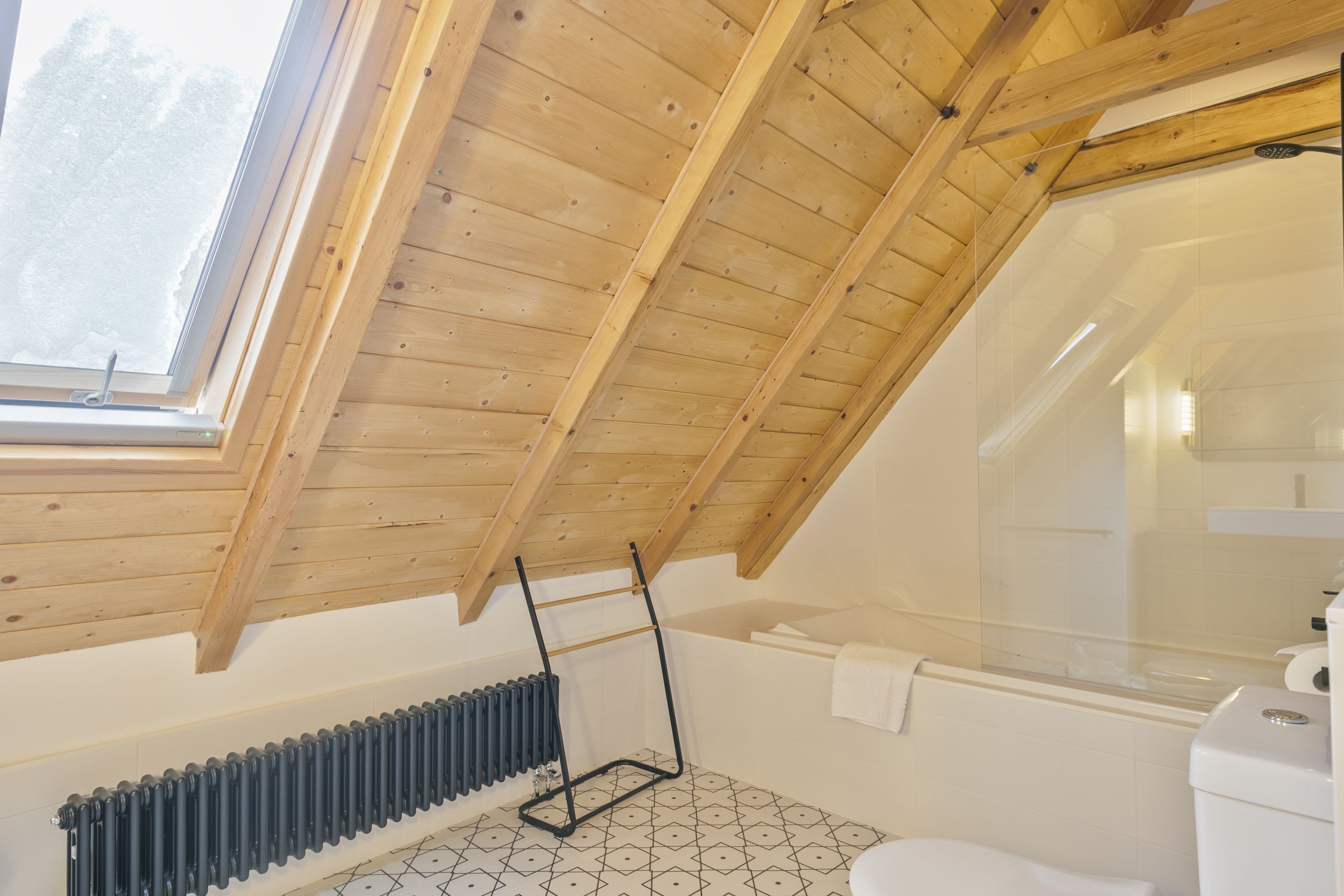 Een badkamer met een schuin houten plafond, een bad, een toilet en een radiator.