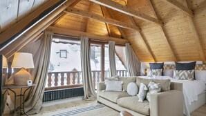 Ein gemütliches Zimmer mit Holzbalkendecke, einer Couch, einem Bett und einem Fenster mit Vorhängen.