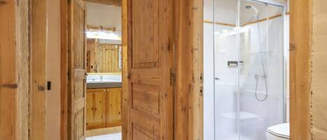 A wooden interior hallway leading to a bathroom with a glass shower enclosure and a toilet.