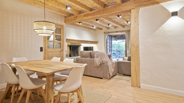 Een gezellige woonkamer met een houten eettafel, witte stoelen, een bank en een open haard.