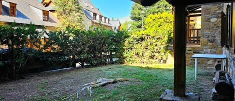 A rustic stone building with a covered outdoor area, surrounded by trees and a grassy yard.