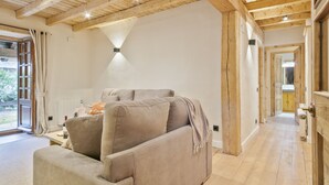 Een gezellige woonkamer met een bank, houten balken in het plafond en uitzicht op het groen.
