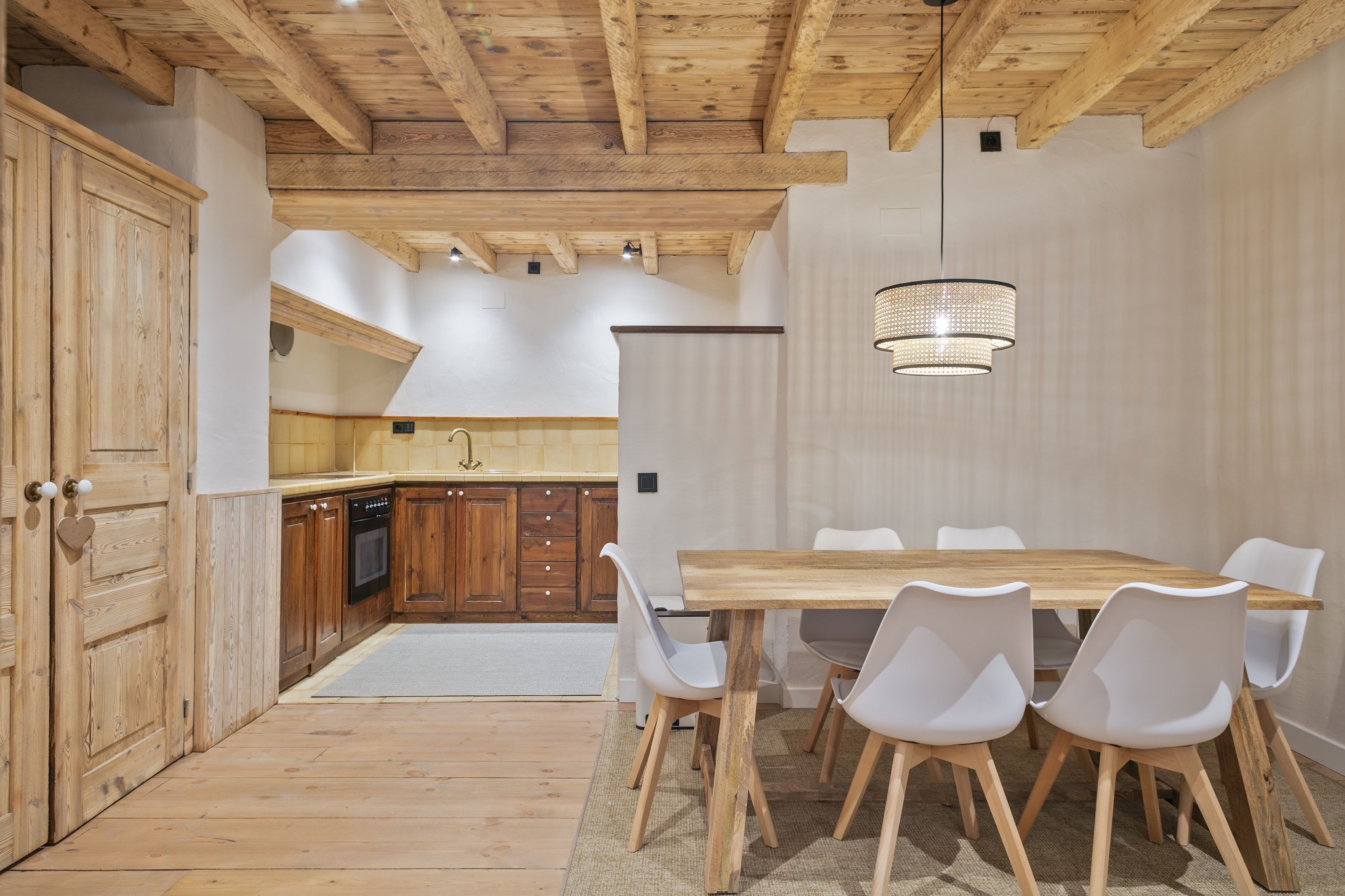 A modern kitchen with wooden cabinets and a dining area with a wooden table and white chairs.