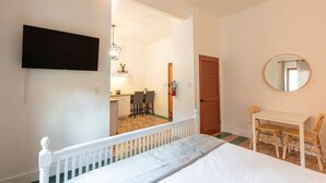 Une chambre à coucher avec un lit, un téléviseur fixé au mur, une petite table avec des chaises et un miroir rond.