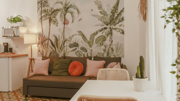 Una sala de estar acogedora con un sofá, una mesa de comedor y un mural grande con motivos tropicales.