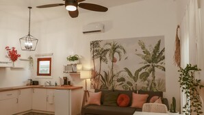 Un espacio habitable compacto con kitchenette, ventilador de techo, comedor y sofá con cojines.