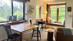 A cozy room with a wooden dining table, a comfortable chair, a sofa with a window seat, and a small wooden stool.
