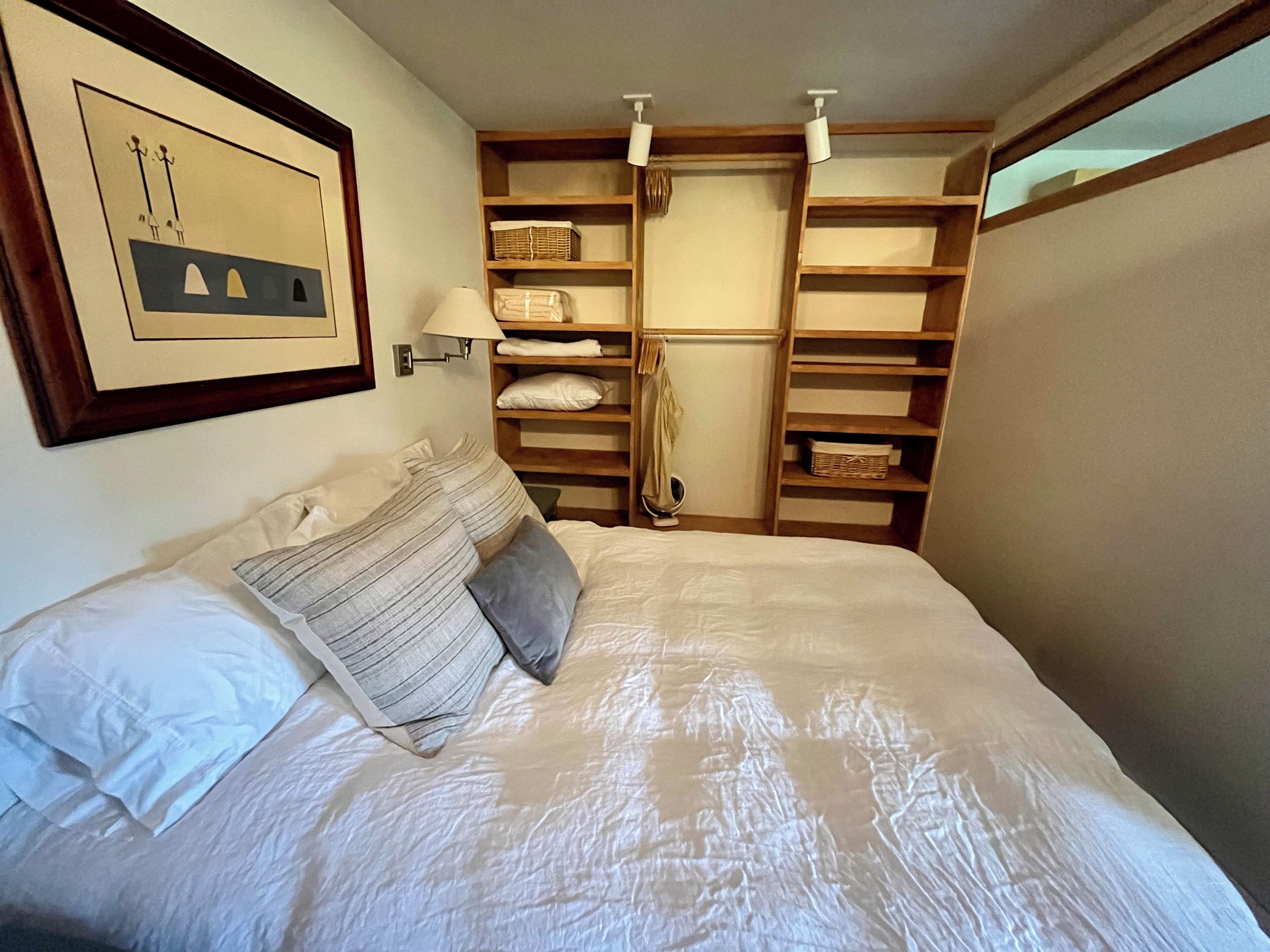 Una cama bien hecha con almohadas, una lámpara fijada a la pared y un cuadro enmarcado.