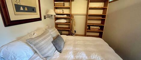 Una cama bien hecha con almohadas, una lámpara fijada a la pared y un cuadro enmarcado.