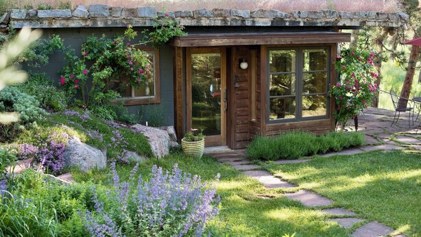 A rustic cabin with a stone roof, wooden door, and large windows.