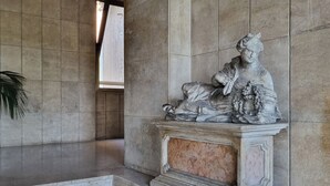 A stone statue of a seated figure with a child, set in a tiled room with a window and a plant. - Rovani 14 - One Bedroom Apartment, Sleeps 3 (Monza)