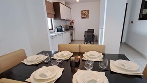 Comedor con una mesa negra dispuesta para seis personas, sillas color beige y una lámpara colgante moderna.