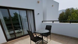 Un balcón con una mesa redonda y dos sillas, una puerta corrediza de cristal y vistas a la vegetación.