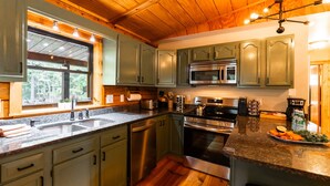 A kitchen with wooden floors, green cabinets, stainless steel appliances, a large window, and a countertop with various items. - Havenbrook~Rustic luxury, 10acres, hot tub (New Plymouth)