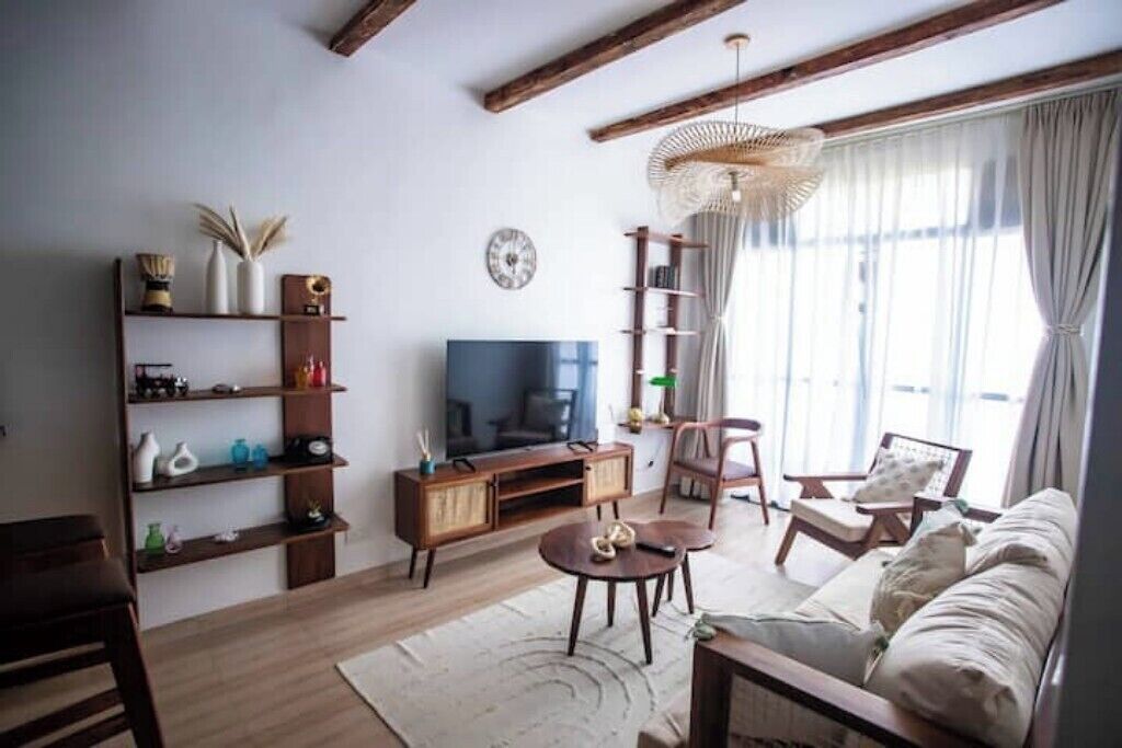 Ein Wohnzimmer mit Fernseher, Holzmöbeln, einer Bücherwand und einem großen Fenster mit Vorhängen.