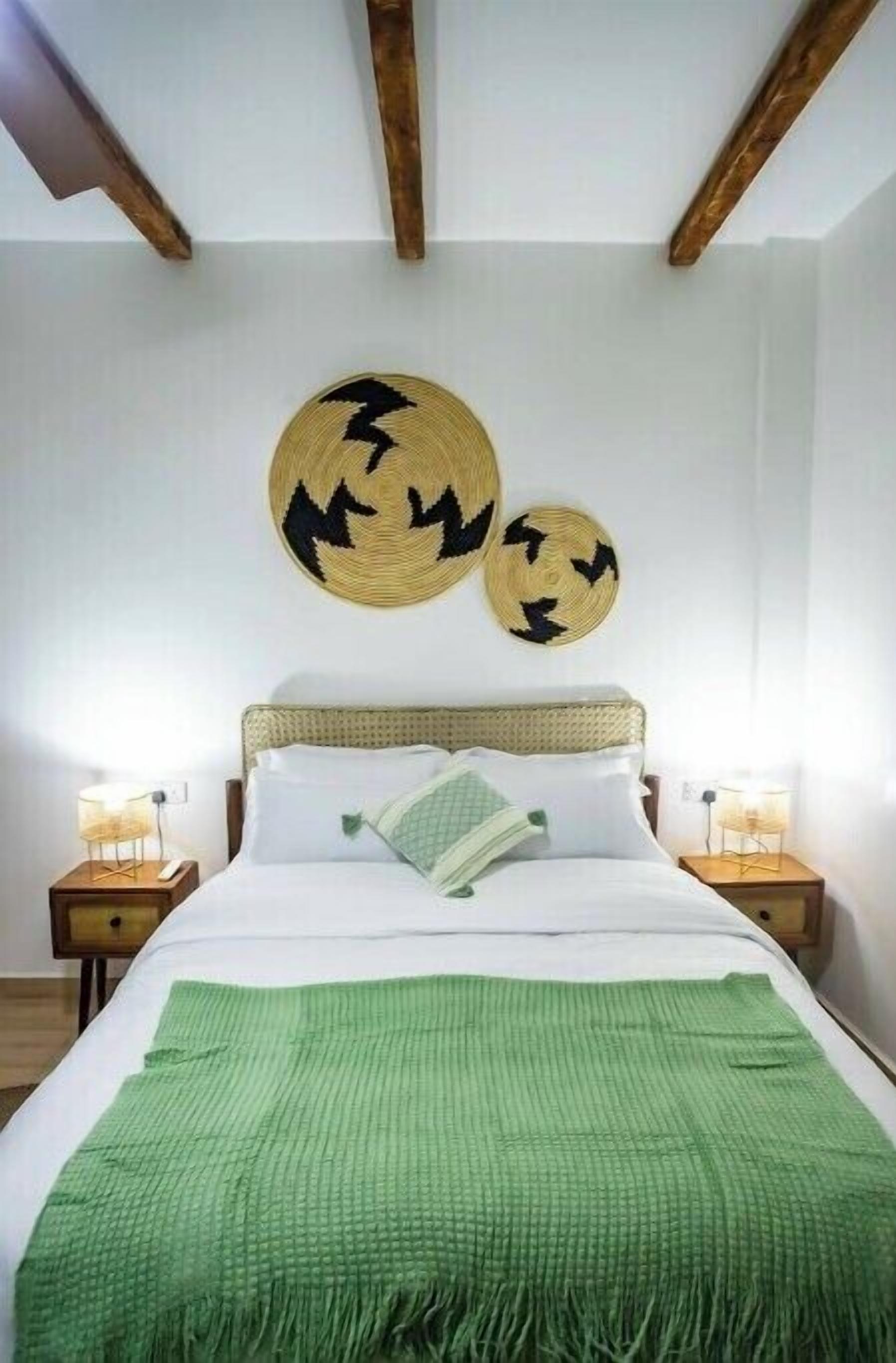Une chambre à coucher comprenant un lit, deux tables de chevet, un plaid vert et deux éléments de décoration murale en fibres tressées.