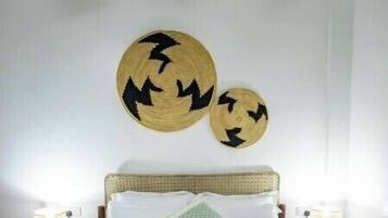Une chambre à coucher comprenant un lit, deux tables de chevet, un plaid vert et deux éléments de décoration murale en fibres tressées.