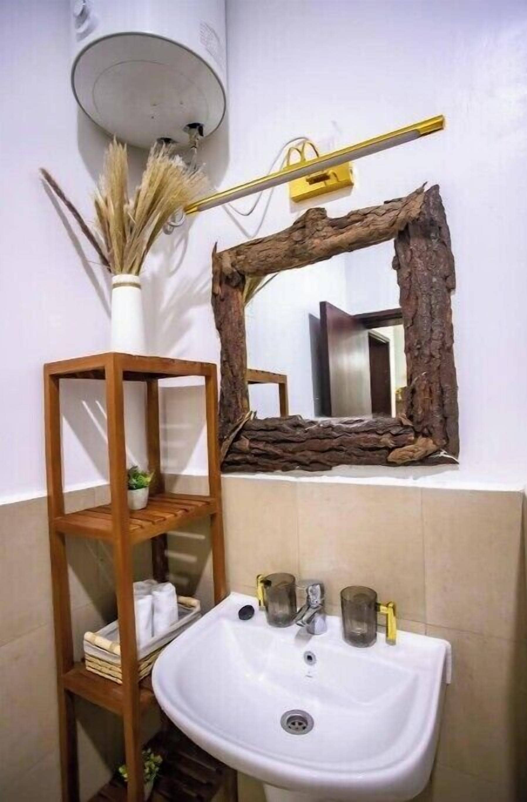Une salle de bain avec une étagère en bois, un lavabo blanc et un miroir doté d’un cadre naturel.