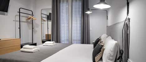 Une chambre d’hôtel moderne, équipée d’un lit, d’une lampe de chevet et offrant une vue sur la ville grâce à de grandes fenêtres.