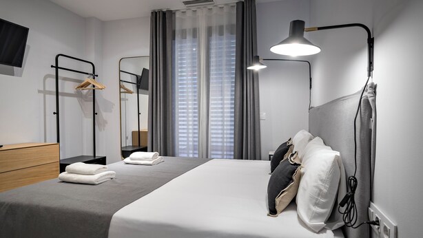 Quarto de hotel moderno com cama, luminária de cabeceira, espelho, armário e televisão de tela plana.
