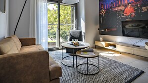 Uma sala de estar moderna com sofá, mesa de centro, televisão e uma janela grande com cortinas.