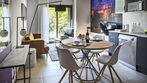 Uma sala de estar moderna com uma mesa de jantar redonda, cadeiras brancas, um sofá marrom e uma janela grande com cortinas.