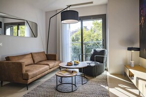 Un saló modern amb un sofà, una taula de centre rodona i una cadira. Hi ha un gran finestral que ofereix vistes a l'exterior.