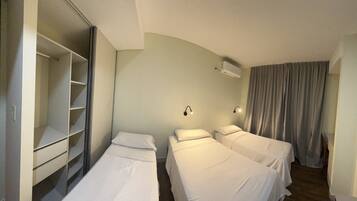 A hotel room with two single beds, a wardrobe, a ceiling-mounted air conditioner, and a curtain on the window.