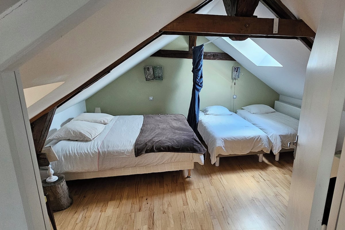 Een kleine zolderkamer met twee bedden, houten vloeren en een schuine plafond met dakraam.