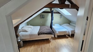 Une petite chambre mansardée avec deux lits, un plancher en bois et un plafond en pente doté d’un puits de lumière.