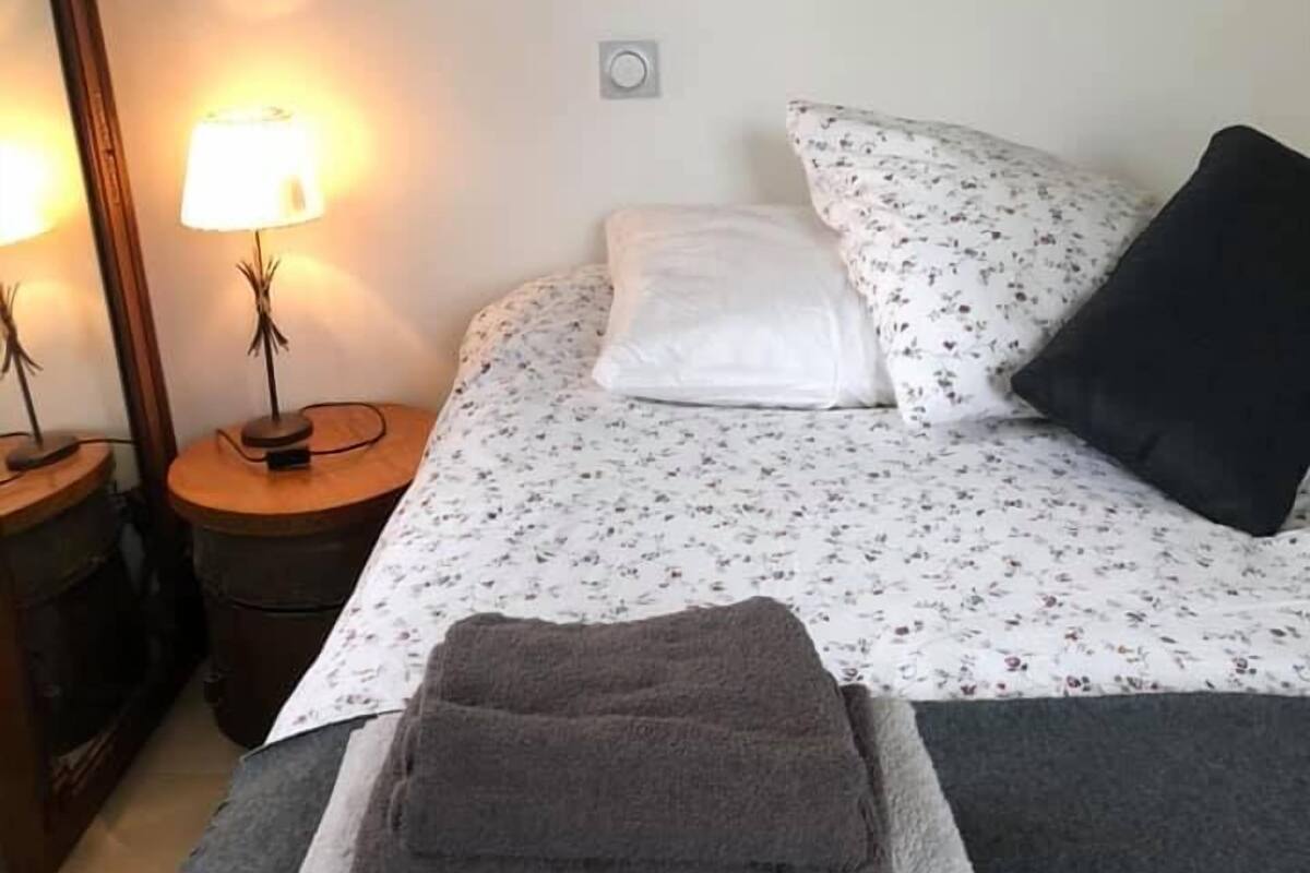 Een netjes opgemaakt bed met een bloemenprintdeken, een ronde spiegel aan de muur en een ingelijst foto erboven.