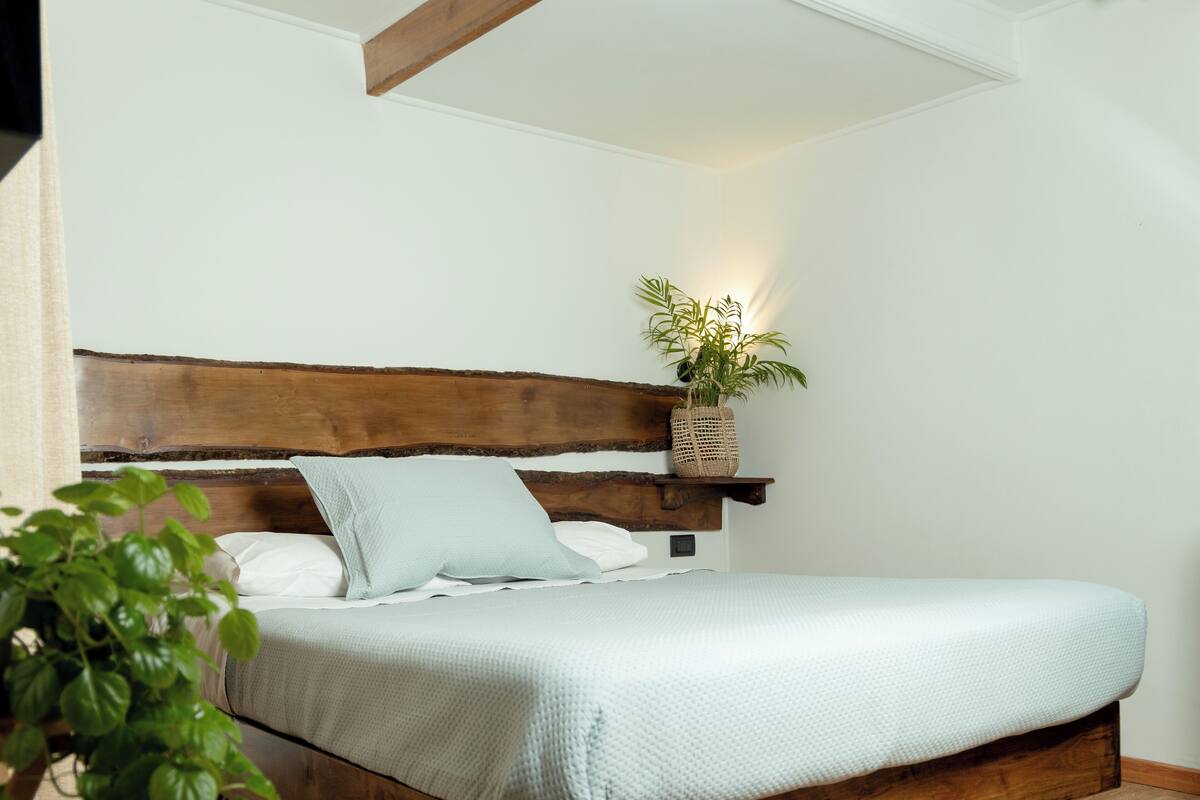 A wooden bed with a white mattress and pillows, a woven basket with a plant on the headboard, and a wooden floor.