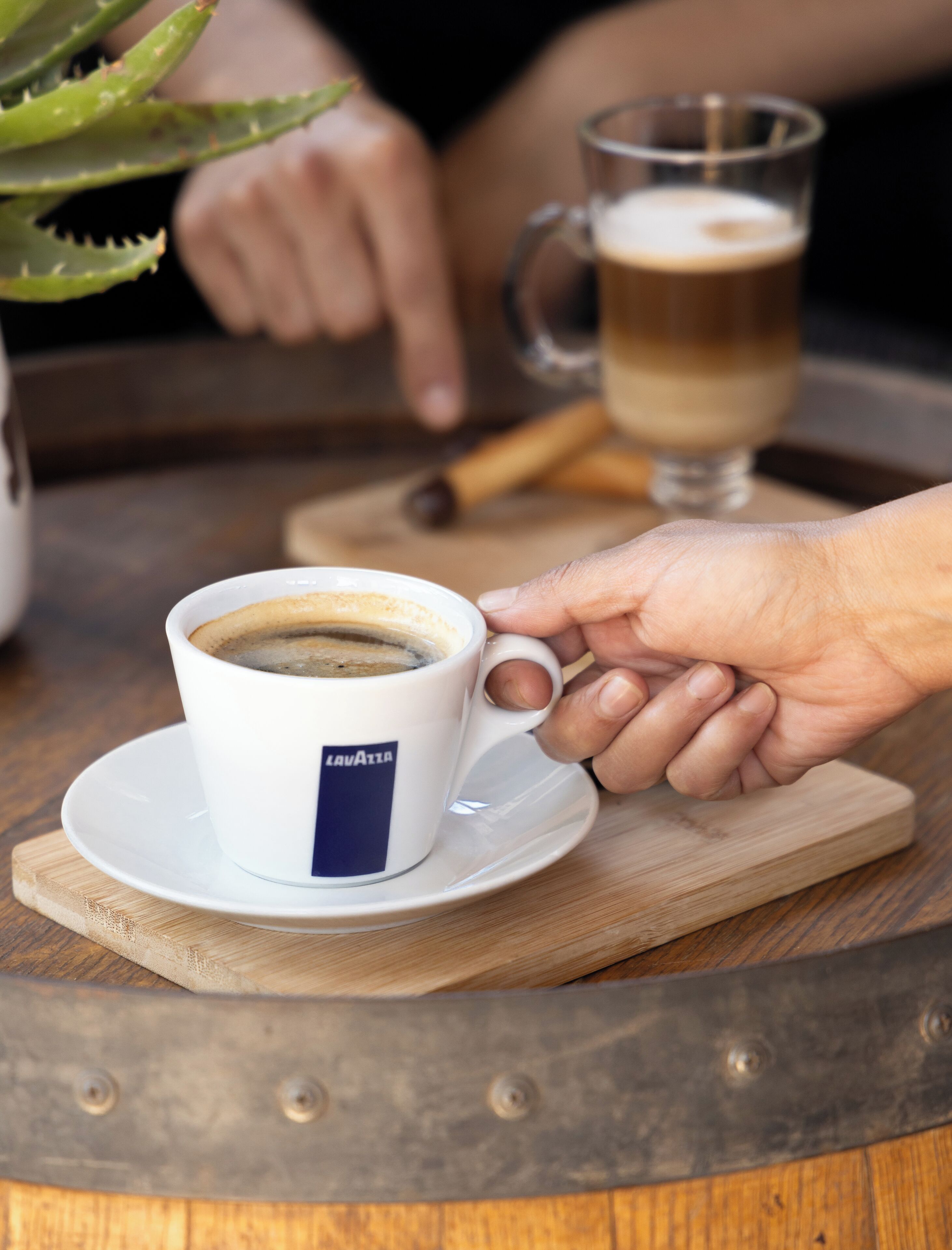 Una taza de café sobre un platito, con una mano apoyada encima.