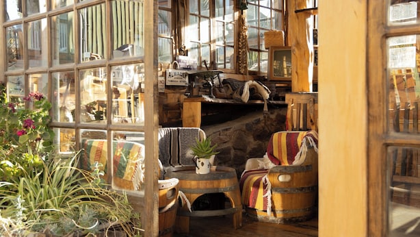 A rustic interior with wooden furniture, a stone wall, and a large window with reflections. - Hotel y Restaurant Doña Rode (Andacollo)