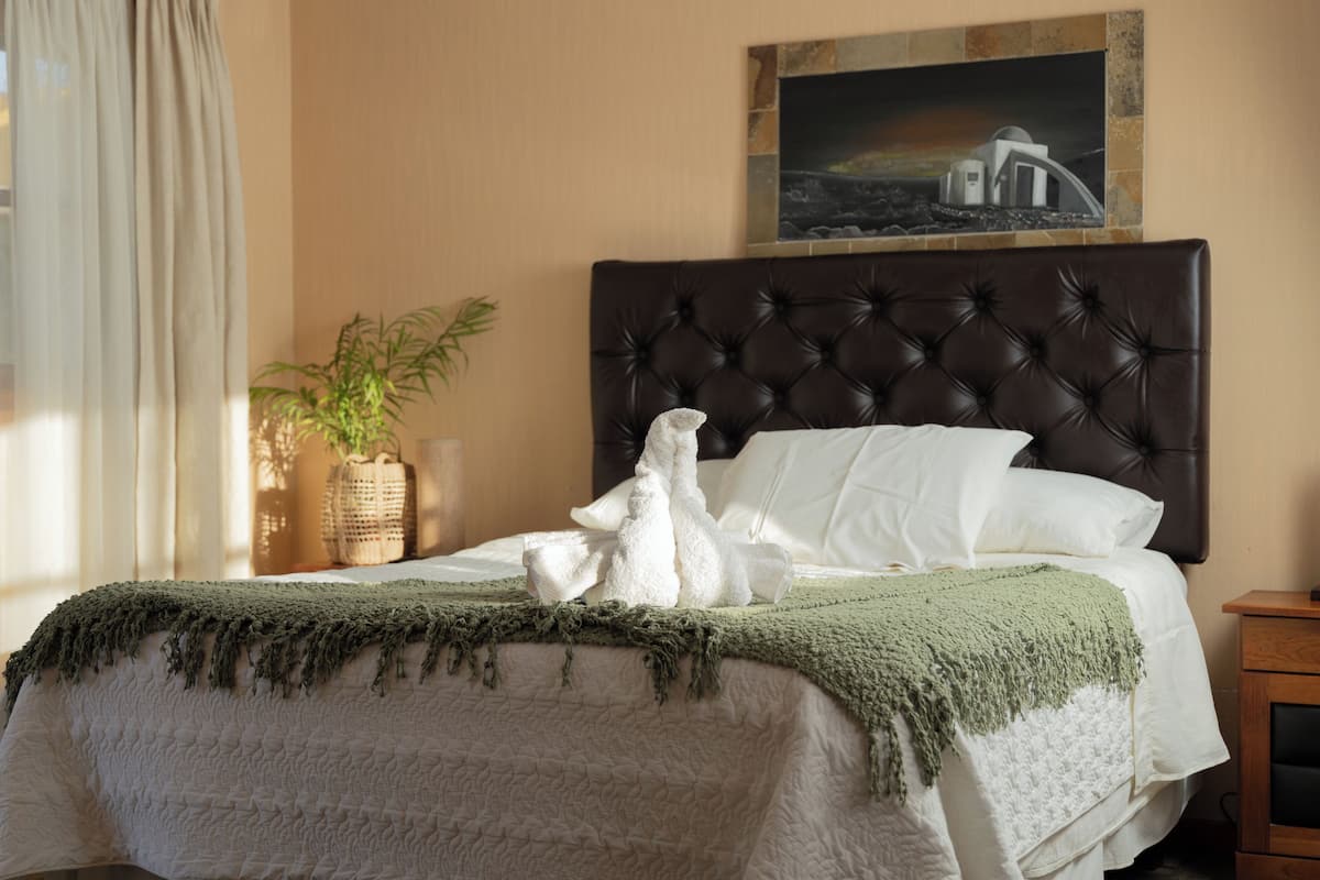 A neatly made bed with a green blanket, a white pillow, and a decorative item on the headboard.