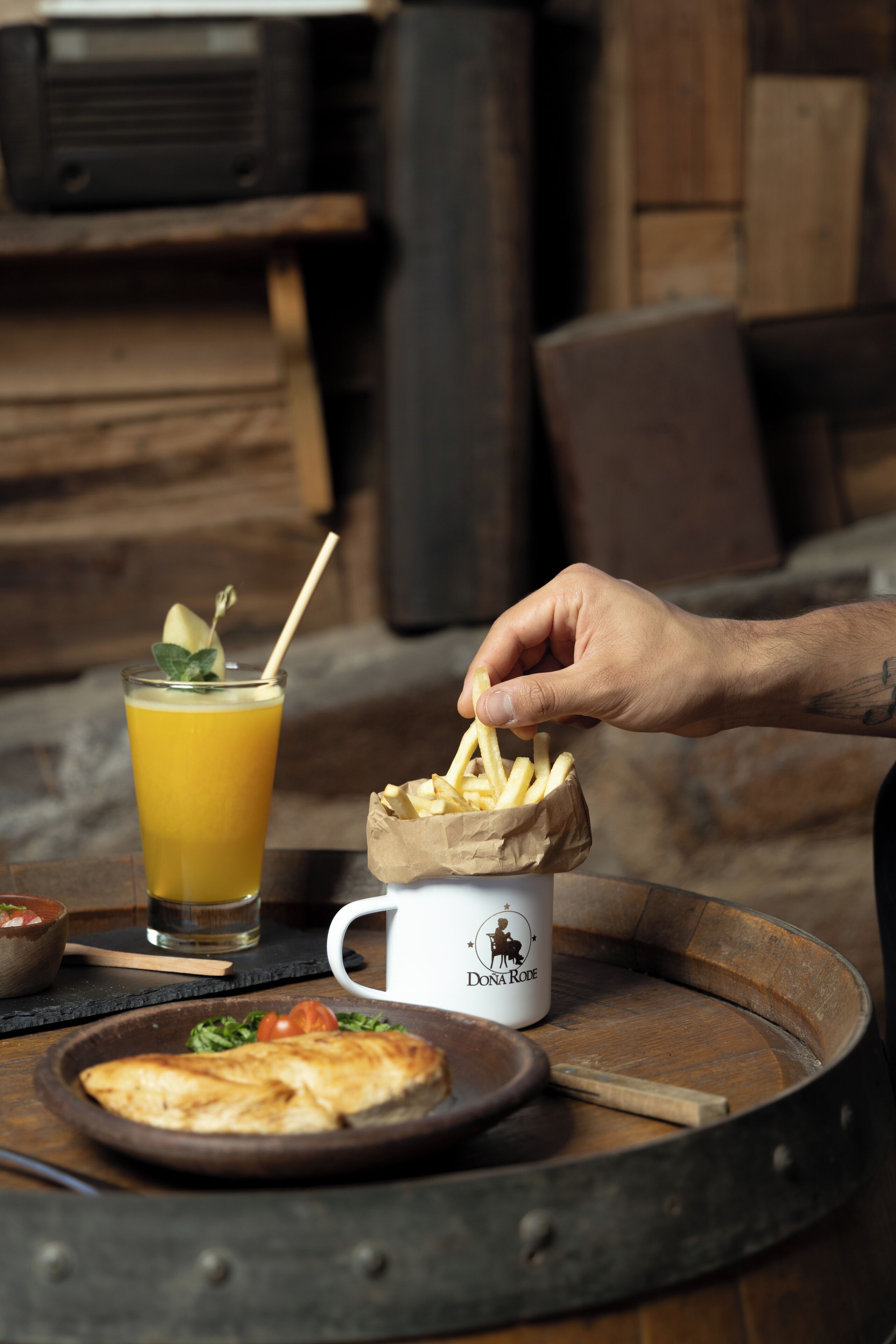 A wooden table with a drink, a plate of fries, and a mug.