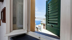 Une fenêtre donnant sur la mer, un balcon avec une balustrade et un immeuble avec un volet vert.