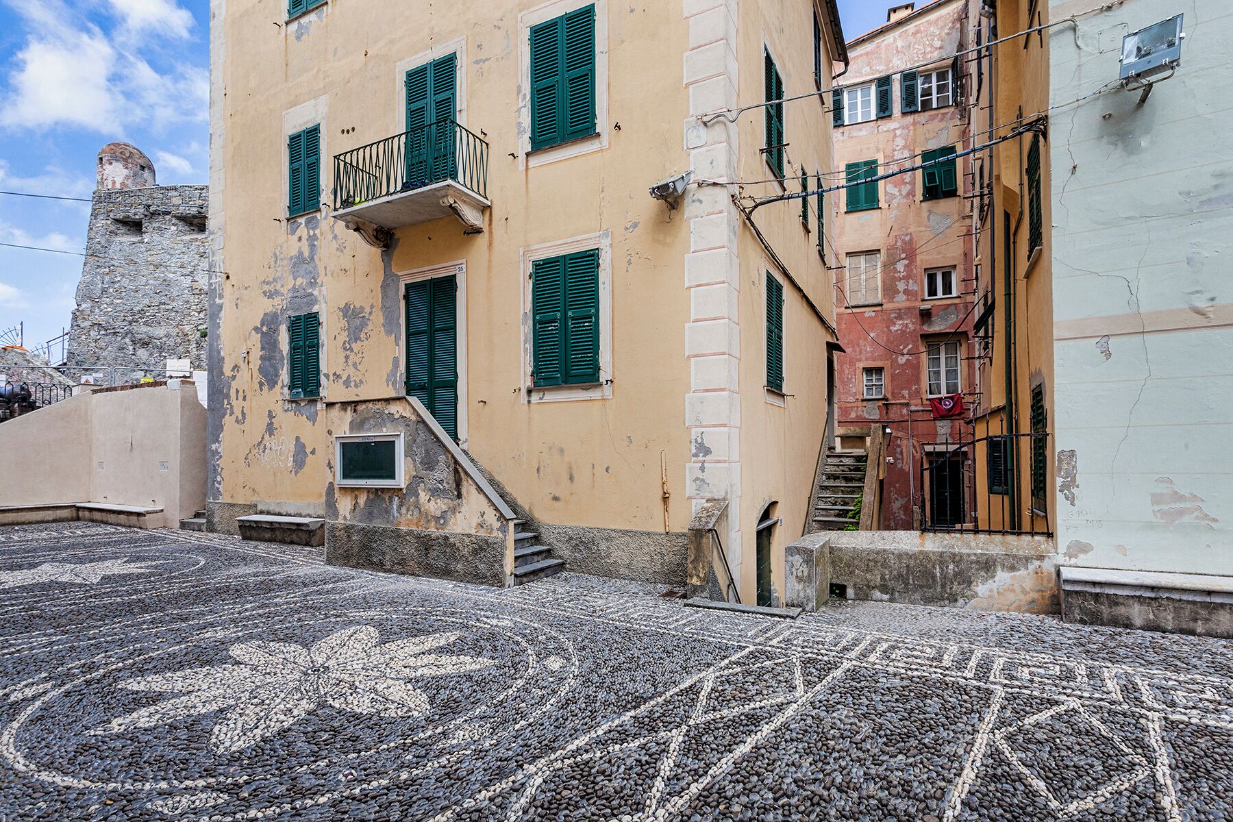 A cobblestone street with buildings featuring balconies and traditional shutters.