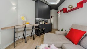 Un salon moderne avec un canapé gris, un coussin rouge et un coin repas comprenant un comptoir de cuisine.